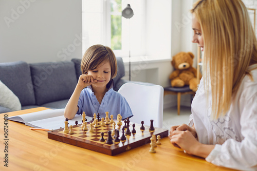 Family hobbies. Young mother playing chess with son at home. Little boy engaged in board game with his parent in room