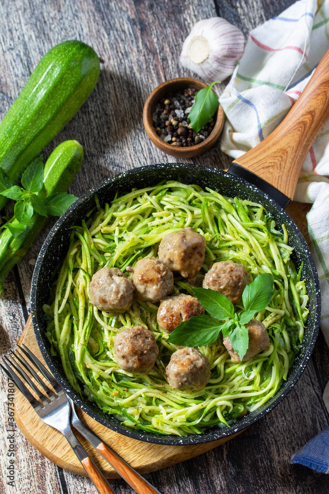 Healthy food. Cooked zucchini noodles with meatballs in a cast iron skillet on a rustic table.