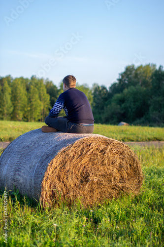 A Young boy sits on a hay bale and enjoys living happy on the country