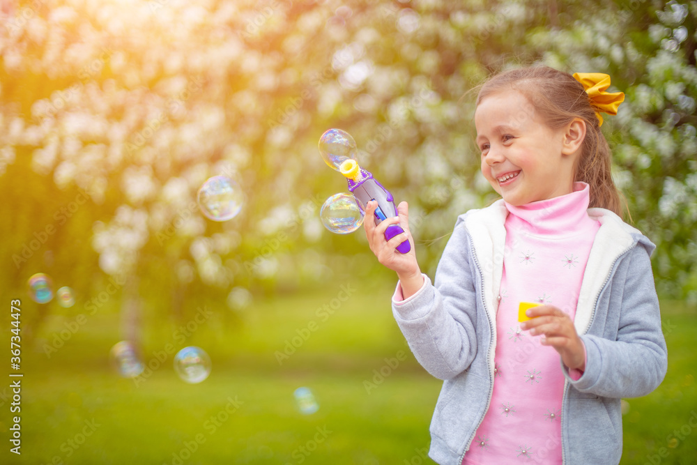 Beautiful little blonde girl, has happy fun cheerful smiling face, soap bubble blower.