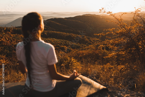 Fototapeta Naklejka Na Ścianę i Meble -  Woman meditating alone on hill with amazing autumn mountain view at sunset. Zen spiritual concept. Praying alone, harmony with nature.