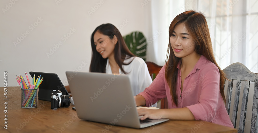 Women are using a computer tablet and laptop while sitting together at the wooden table. Women are using a computer tablet and laptop while sitting together at the wooden table.