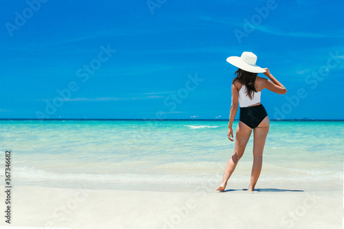 Seascape on a tropical island with white sand and blue sky. A girl stands on the seashore. Travel vacation concept