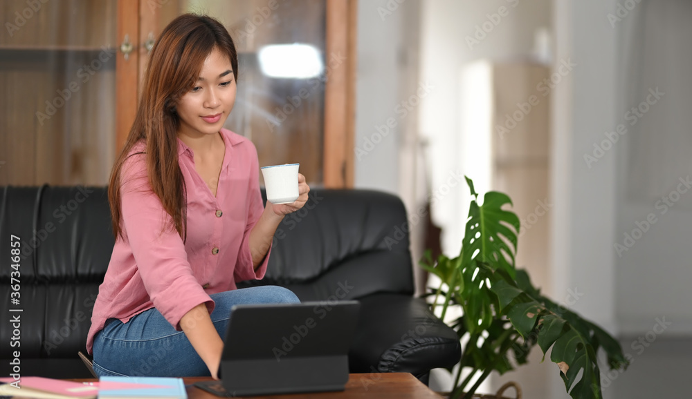 A beautiful woman is relaxing with a computer tablet while sitting on a black sofa.