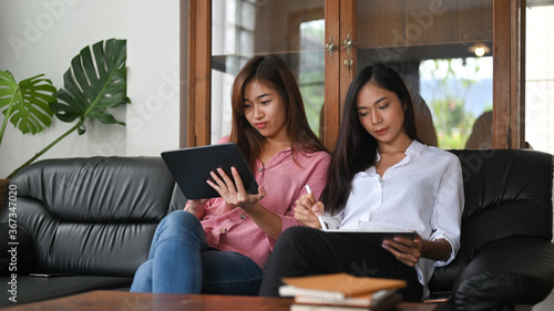Asian women are sitting and relaxing with a computer tablet on the black leather sofa.