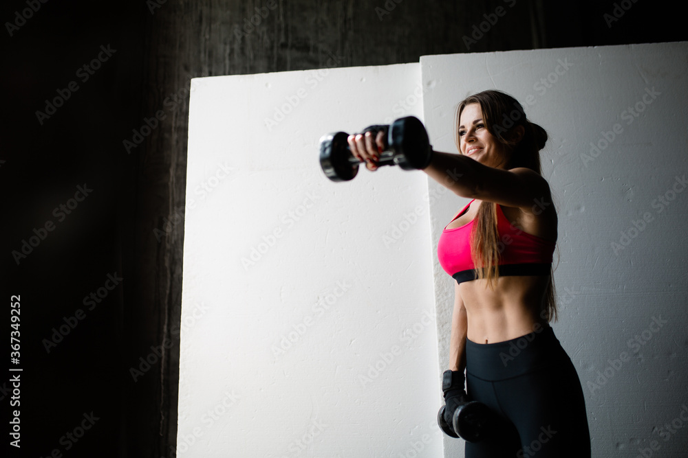 Beautiful girl Kickboxing trainer trains with dumbbells in hands alternately stretching her arms in front of her on a white background