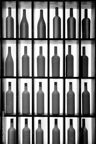 Black and white image. Identical white bottles of alcohol are placed on a shelf with a back light. Silhouettes and decor