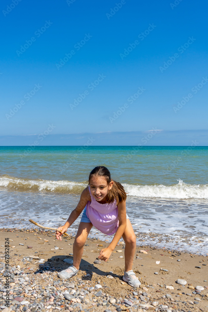 Little girl dressed in pastel colors jumping and playing on the stone and sandy shore of the Mediterranean Sea