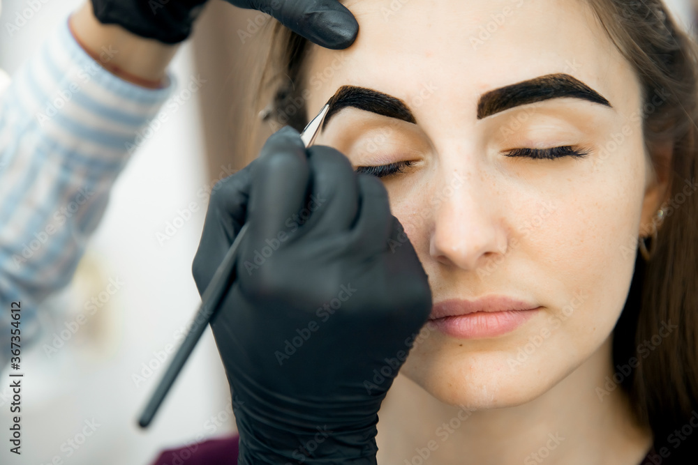 Correction and tinting eyebrows, master applies thread to woman on brow Correction and tinting eyebrows, master applies thread to woman on brow