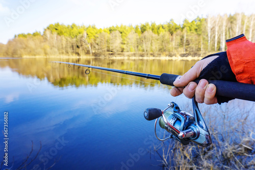 Summer fishing on a predator. Hand with a spinning rod on a background of nature. Close-up