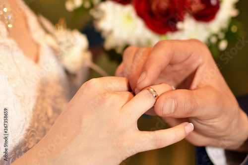 The groom puts a golden wedding ring on the bride's finger, close-up