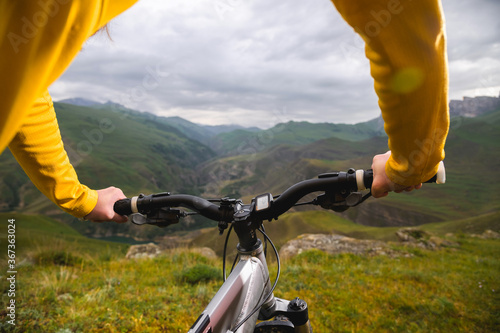 A close-up of the girl's hand cyclist on the handlebars of a mountain bike against the backdrop of epic rocks and mountains. Mountain bike. Girls cyclist