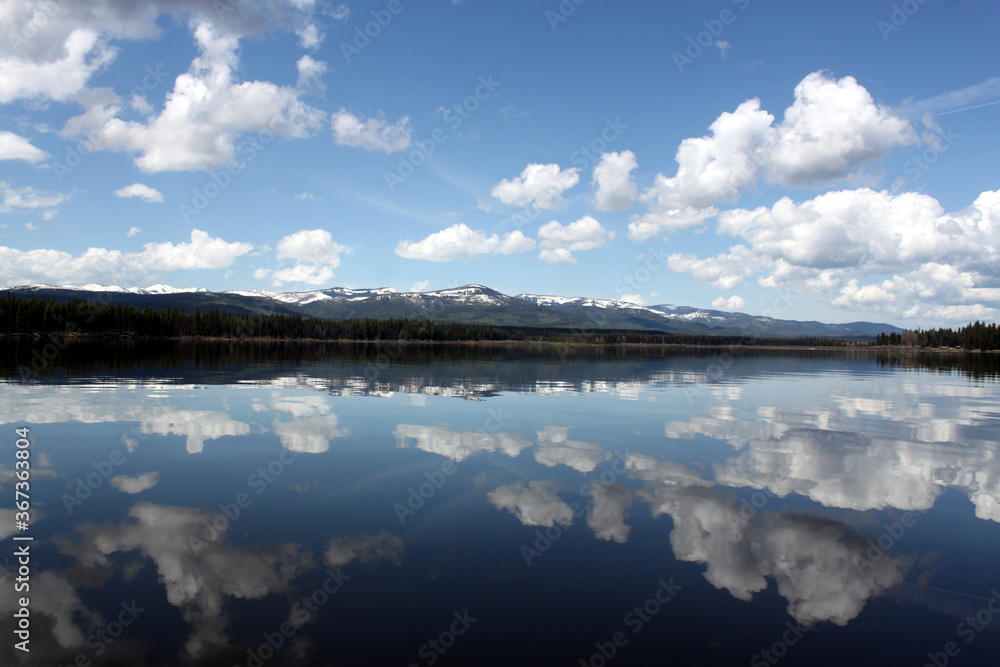 Dynamic cloudy blue skies over mountains, grassy fields, and calm water