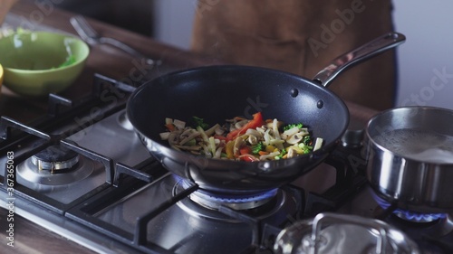 Woman frying vegetables in wok pan at home