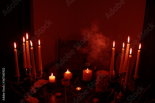 Fototapeta in a dark room on a round esoteric table candles burn, smoke, animal skulls lie,