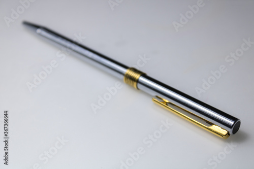 metal pen, with golden and silver colors, in a transversal position, on a white surface