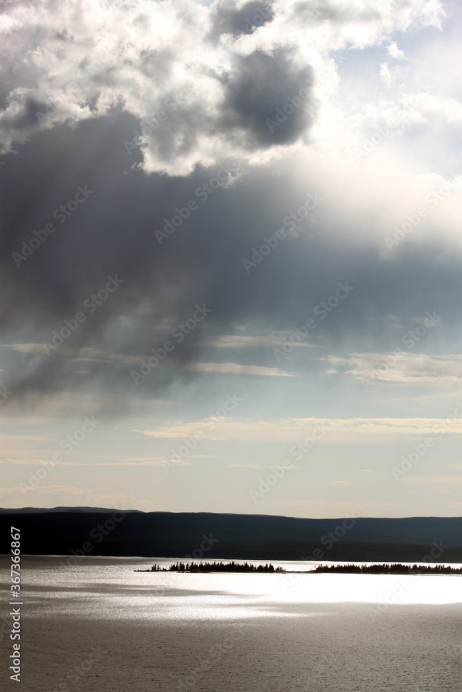Dynamic cloudy blue skies over mountains, grassy fields, and calm water Dynamic cloudy blue skies over mountains, grassy fields, and calm water