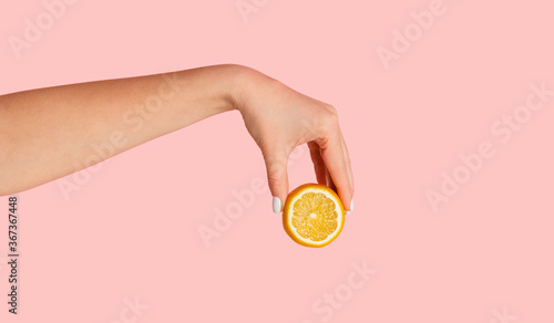Unrecognizable millennial girl showing cut orange fruit over pink background, closeup of hand