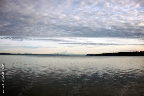 Seascape and shoreline with dynamic cloudy blue skies with reflections in calm water