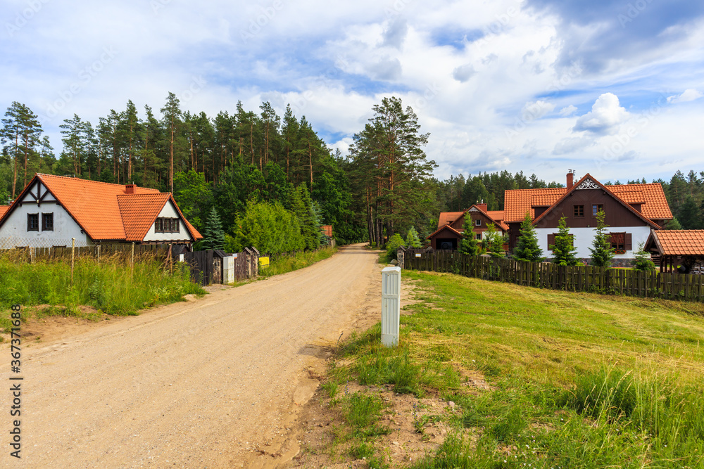 Rural road and traditional style rustic houses in Wygryny village near lake Nidzkie, Mazury Lake District, Poland