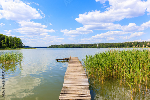 Fototapeta Naklejka Na Ścianę i Meble -  Wooden pier and grass on lake Nidzkie shore on sunny summer day with beautiful clouds on blue sky, Mazury Lake District, Poland