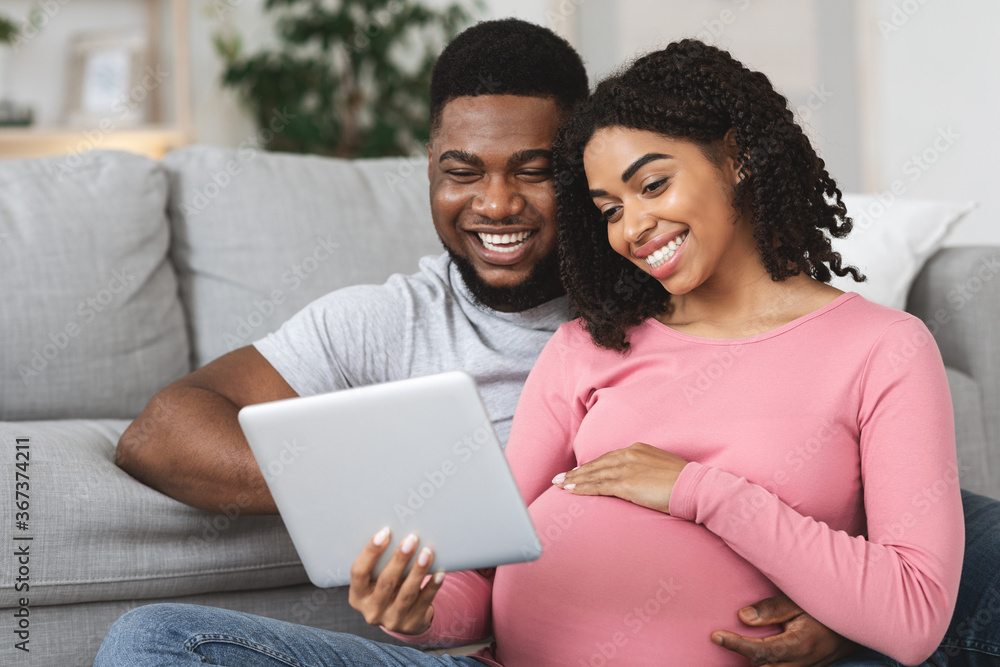 Fototapeta premium Pregnant couple having fun at home, using digital tablet together