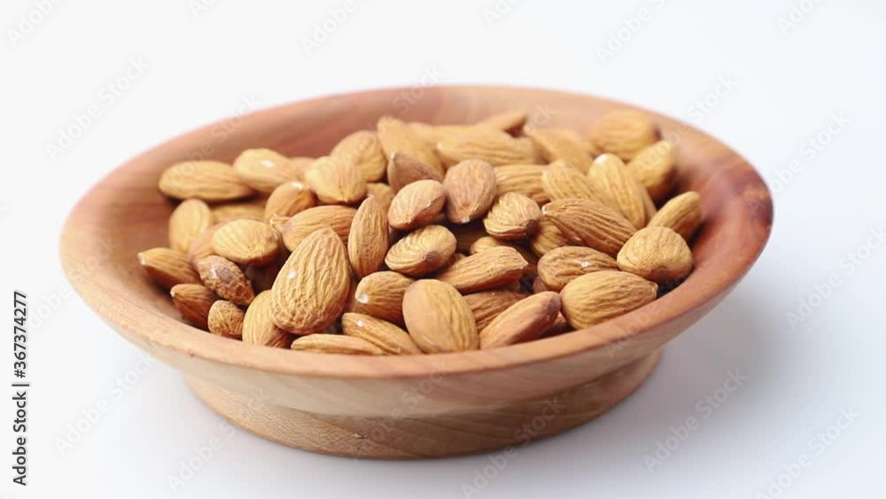 Rotating of almonds in wooden plate on white background. Side view, close up. Rotating of almonds in wooden plate on white background. Side view, close up.