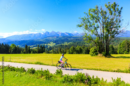 Young female biker cycling along Tatra Mountains on beautiful summer sunny day at Lapszanka Pass, Poland