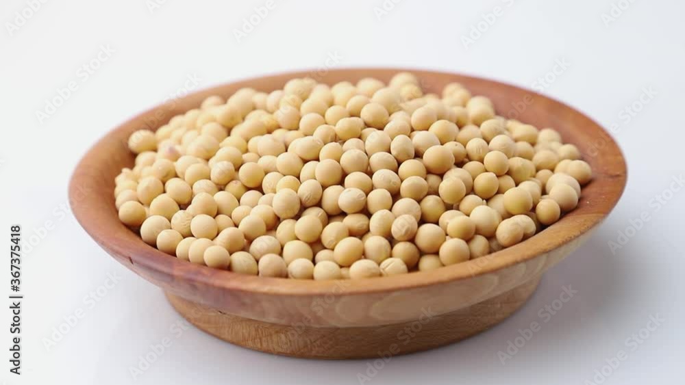 Rotating of soy seeds in wooden plate on white background. Side view, close up. Rotating of soy seeds in wooden plate on white background. Side view, close up.