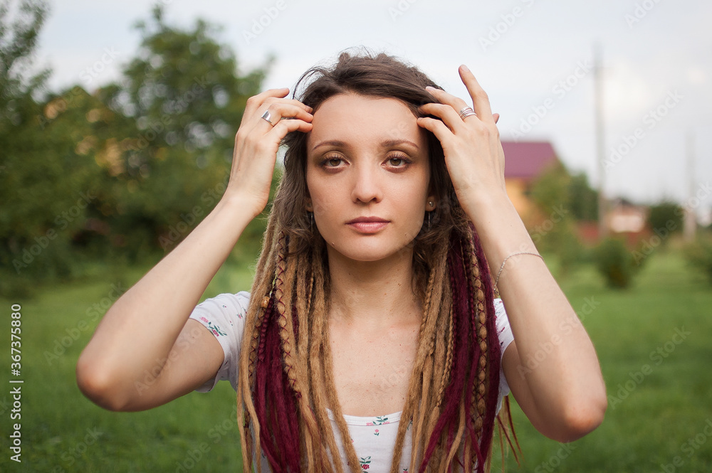 Outdoors female portrait of a modern girl with dreadlocks wearing white shirt in a city park during a sunset, be free, be youself concept
