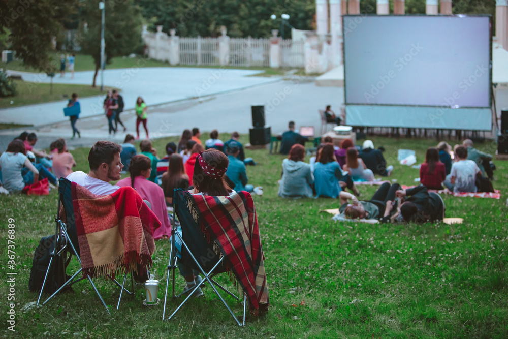 Fototapeta premium couple sitting in camp chairs in front of movie screen at open air cinema