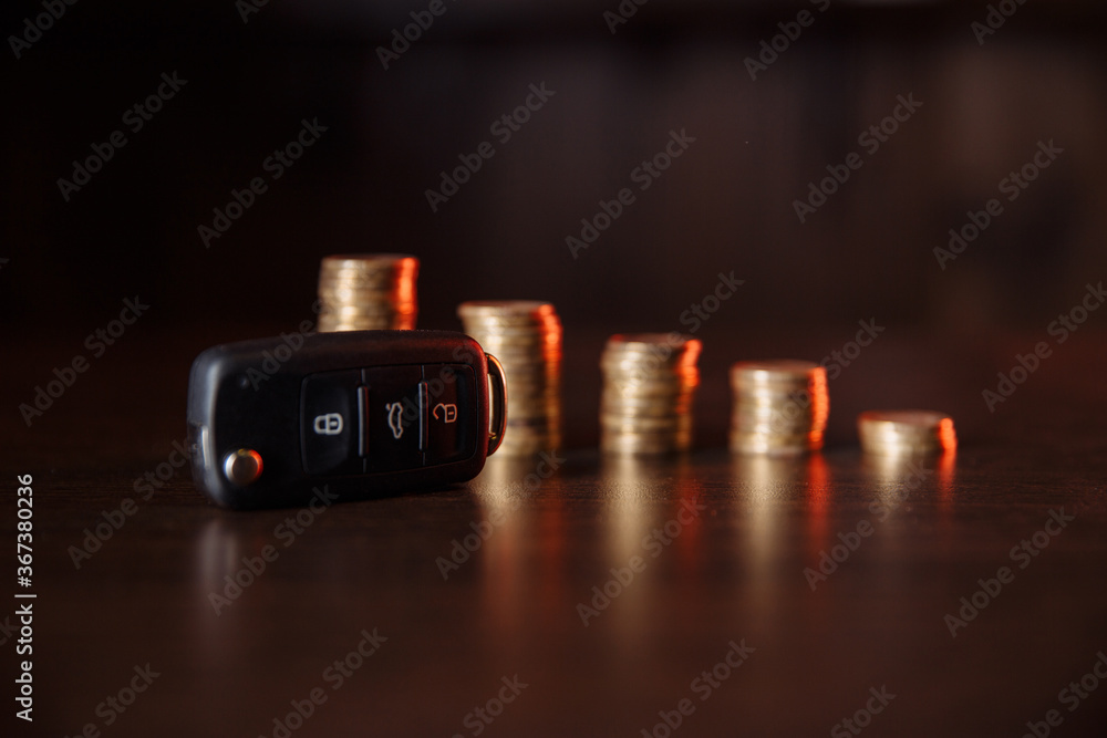 Close-up of car key in front of coins stacked on wooden table. Saving money concept.