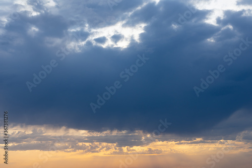 Dramatic rainy clouds on orange and dark blue evening sky. Natural background with stormclouds and sunlights of setting sun.