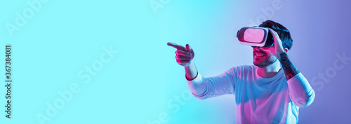 Acquaintance with virtual world. Smiling guy with glasses points finger in neon