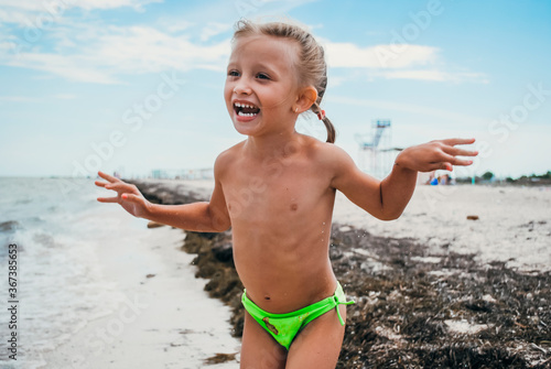 Girl laughing on the beach in sunny day, as summertime activity with young girl. Holiday in summer days with happiness and emotions. Blue sky and sand coastline on the background.