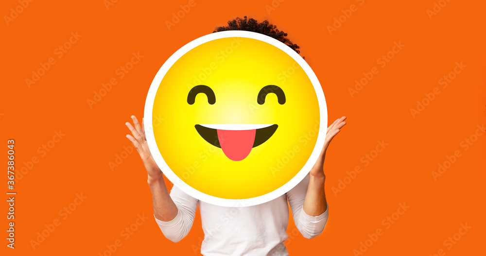 Black bushy man holding happy cheeky emoji emoticon in front of head Black bushy man holding happy cheeky emoji emoticon in front of head