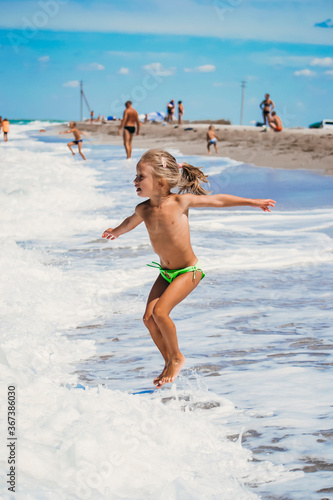 Small girl jump above the waves, happiness of summertime and holiday in summer period. Sand coastline and white waves on the beach. Enjoy of summer days with girl.