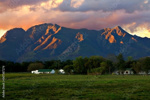 Canvas Print landscape view of the sun setting on a farm house at the base of the outeniqua m