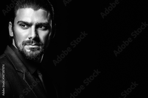 Business portrait of a white caucasian man in a black classic suit on a black background. Bearded man looks confident eyes.