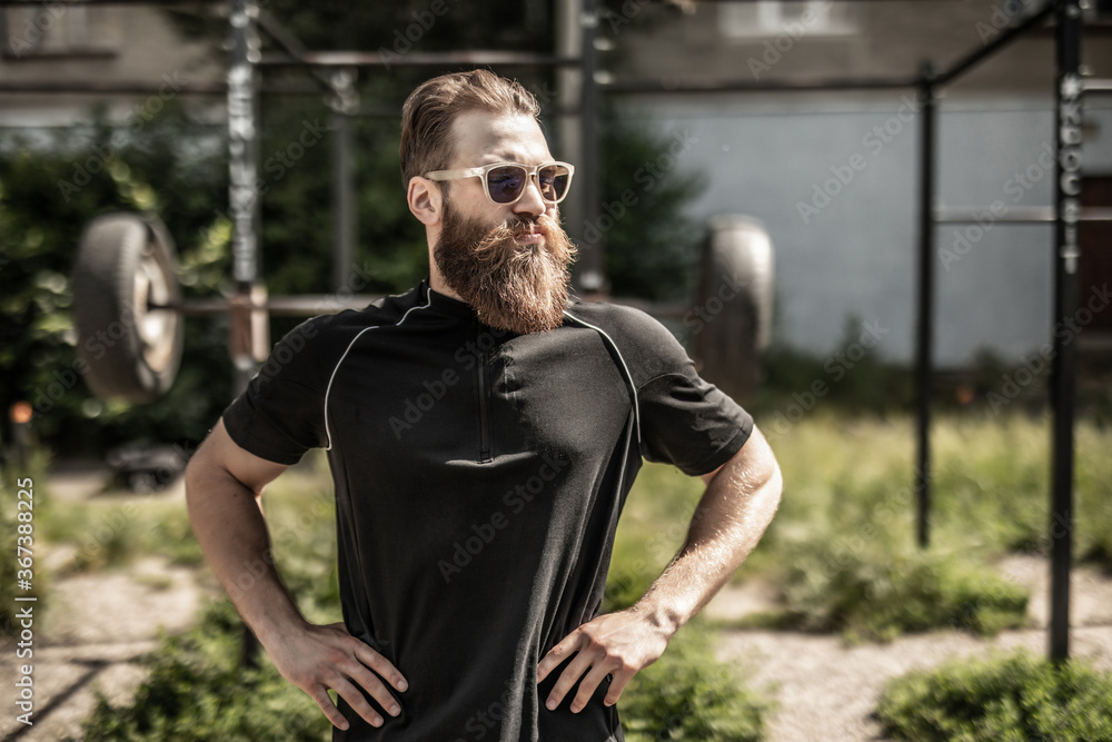 Fototapeta premium Confident muscular young man standing with arms crossed outdoors.