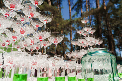 Drink coctkail catering for wedding. Big pyramid of glasses with champagne and red cherry inside on business meeting at summer day in the forest. photo