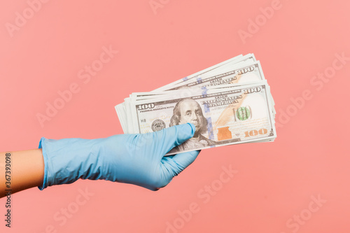 Profile side view closeup of human hand in blue surgical gloves holding and showing fan of american dollar money in hand. indoor, studio shot, isolated on pink background.
