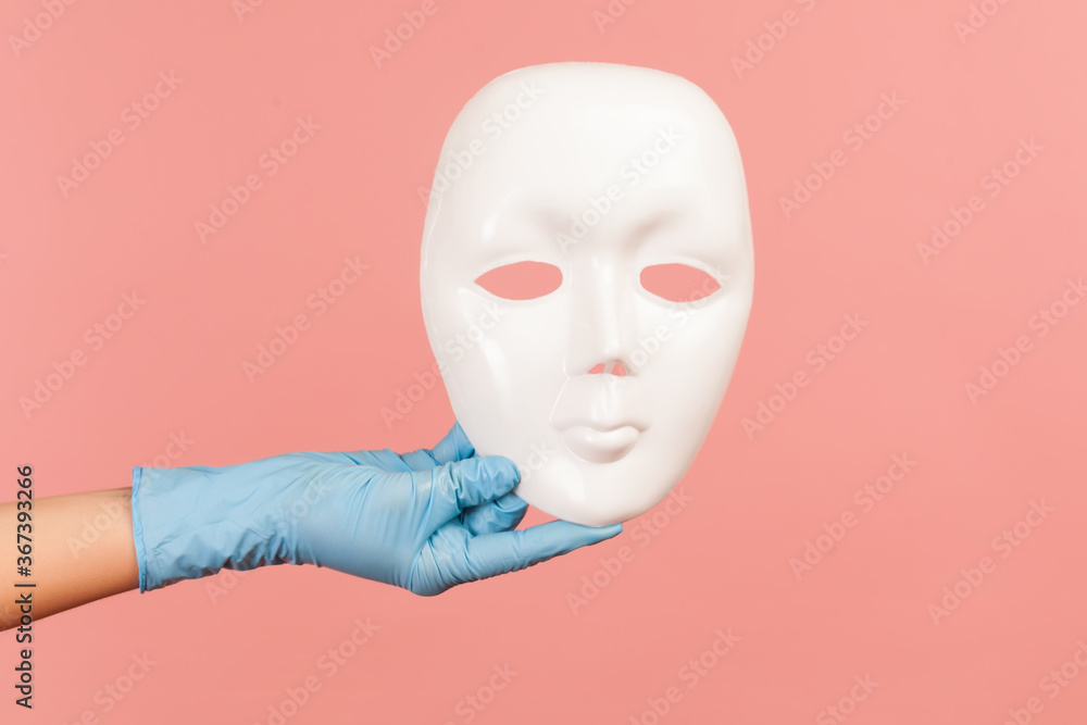 Profile side view closeup of human hand in blue surgical gloves holding white facial mask model. indoor, studio shot, isolated on pink background. Profile side view closeup of human hand in blue surgical gloves holding white facial mask model. indoor, studio shot, isolated on pink background.