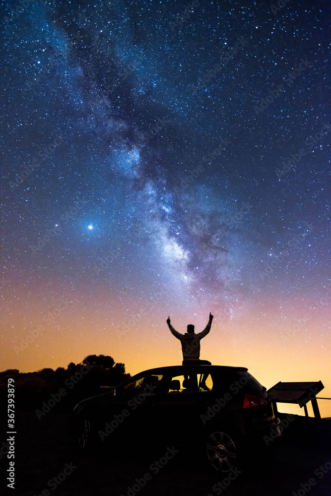 Silhouette of a man with his arms raised looking at the stars and the Milky Way on a summer night in the sky of Tenerife