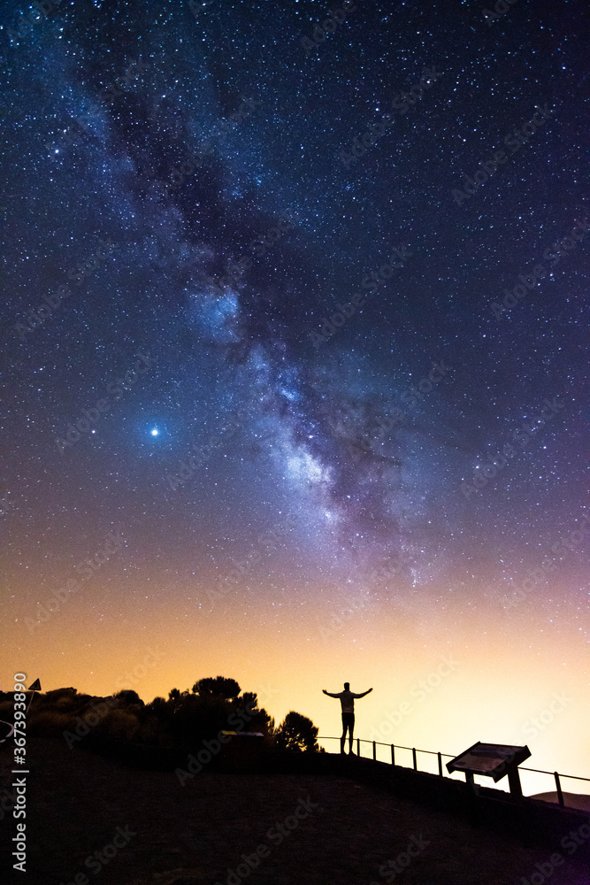 Silhouette of a man with his arms raised looking at the stars and the Milky Way on a summer night in the sky of Tenerife