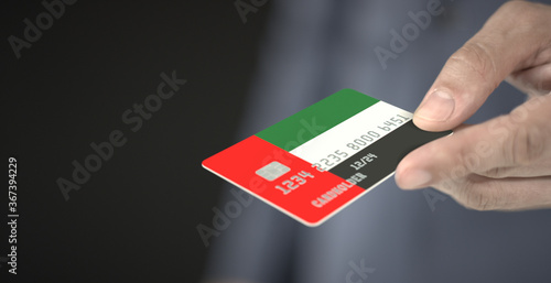 Man offers plastic bank card with printed flag of the United Arab Emirates. Fictional numbers