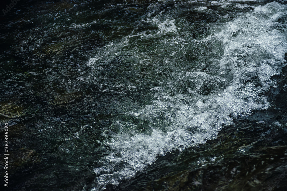 Nature background of dark water stream of mountain river with rapids. Full frame of sea surf. Natural textured backdrop of ocean surf. Texture of tide close-up. Dark water surface of mountain creek.