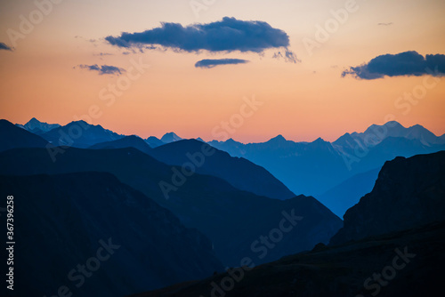 Colorful dawn landscape with beautiful mountains silhouettes and golden gradient sky with blue clouds. Vivid mountain scenery with picturesque multicolor sunset. Scenic sunrise view to mountain range.