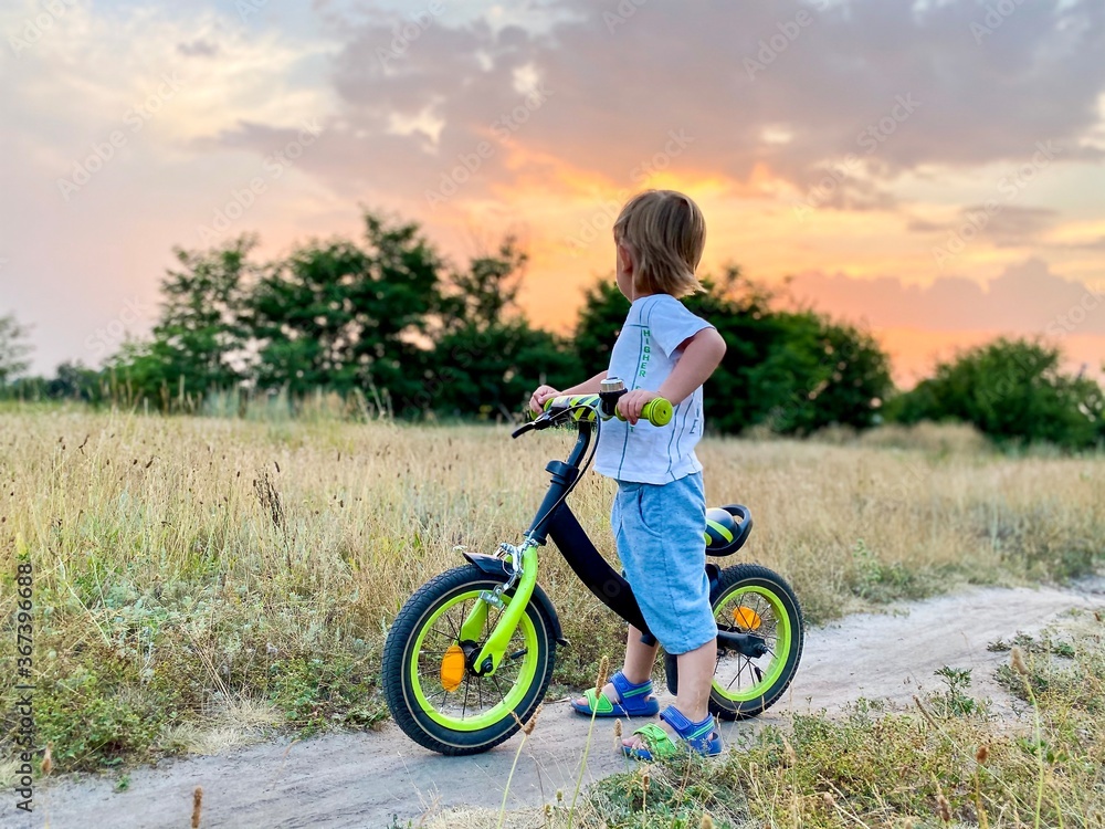 Little light-skinned child on a bright bike ride, rides across the field at sunset in summer. Free space.Active lifestyle concept. Little light-skinned child on a bright bike ride, rides across the field at sunset in summer. Free space.Active lifestyle concept.