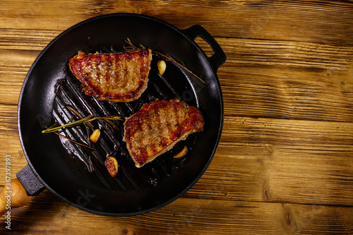 Grilled pork steaks with rosemary, garlic and spices in cast iron grill frying pan on wooden table. Top view
